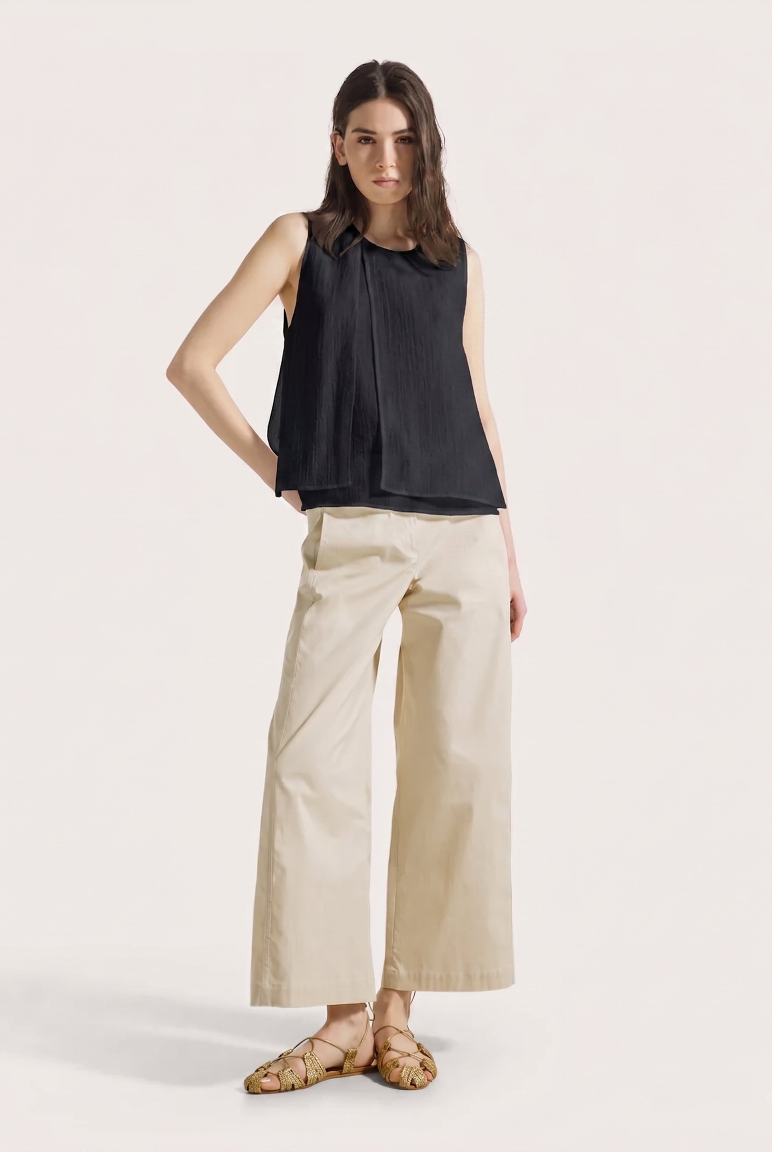 Woman wearing a black sleeveless top and beige wide-leg pants on a white background
